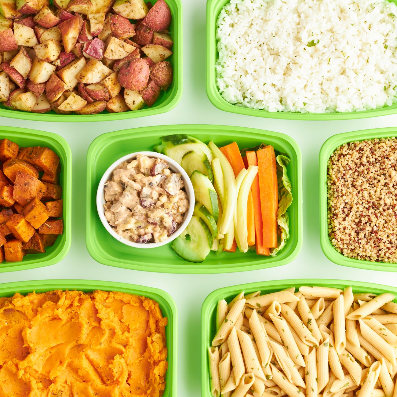A vibrant flat lay of nutritious meal preps including pasta, vegetables, and grains in green containers.