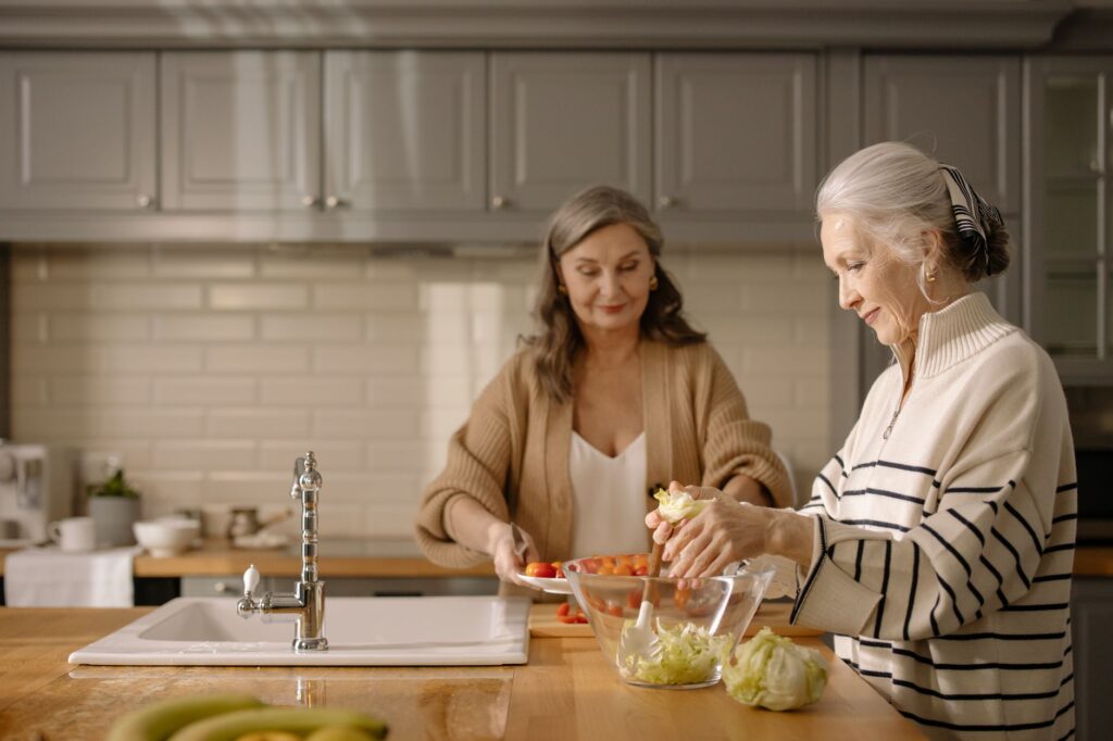Two senior women making a fresh salad together in a cozy kitchen setting.