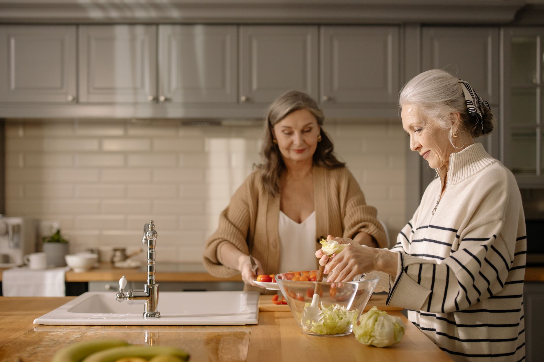 Two senior women making a fresh salad together in a cozy kitchen setting.